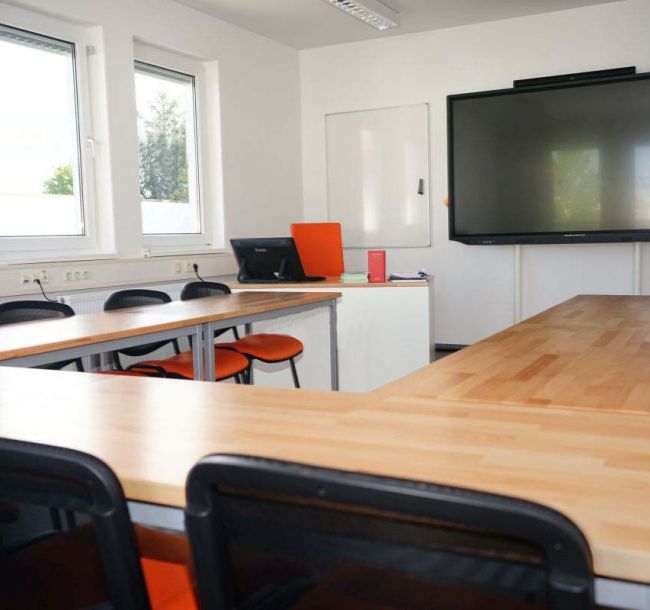 Schulungsraum mit Fenstern, Bildschirm, Tischen und Stühlen