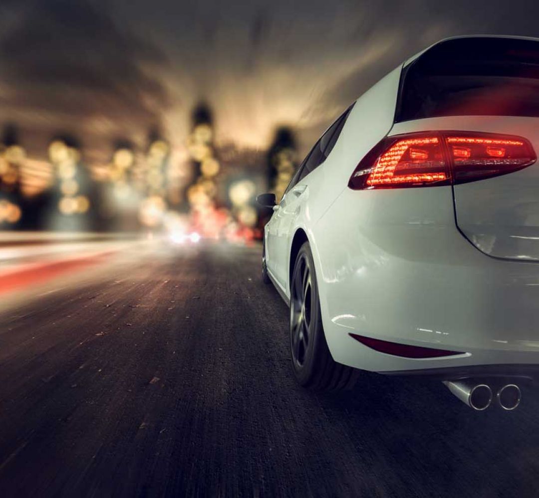 weißes Auto Heckansicht mit Zoomeffekt auf dahinterliegende, nächtliche Stadt